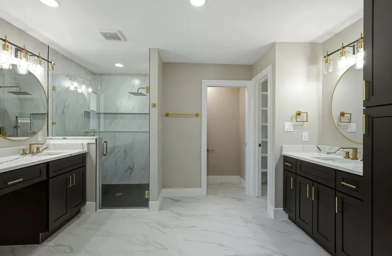 Master bathroom with twin dark vanities, marble effect tile and round gold framed mirrors