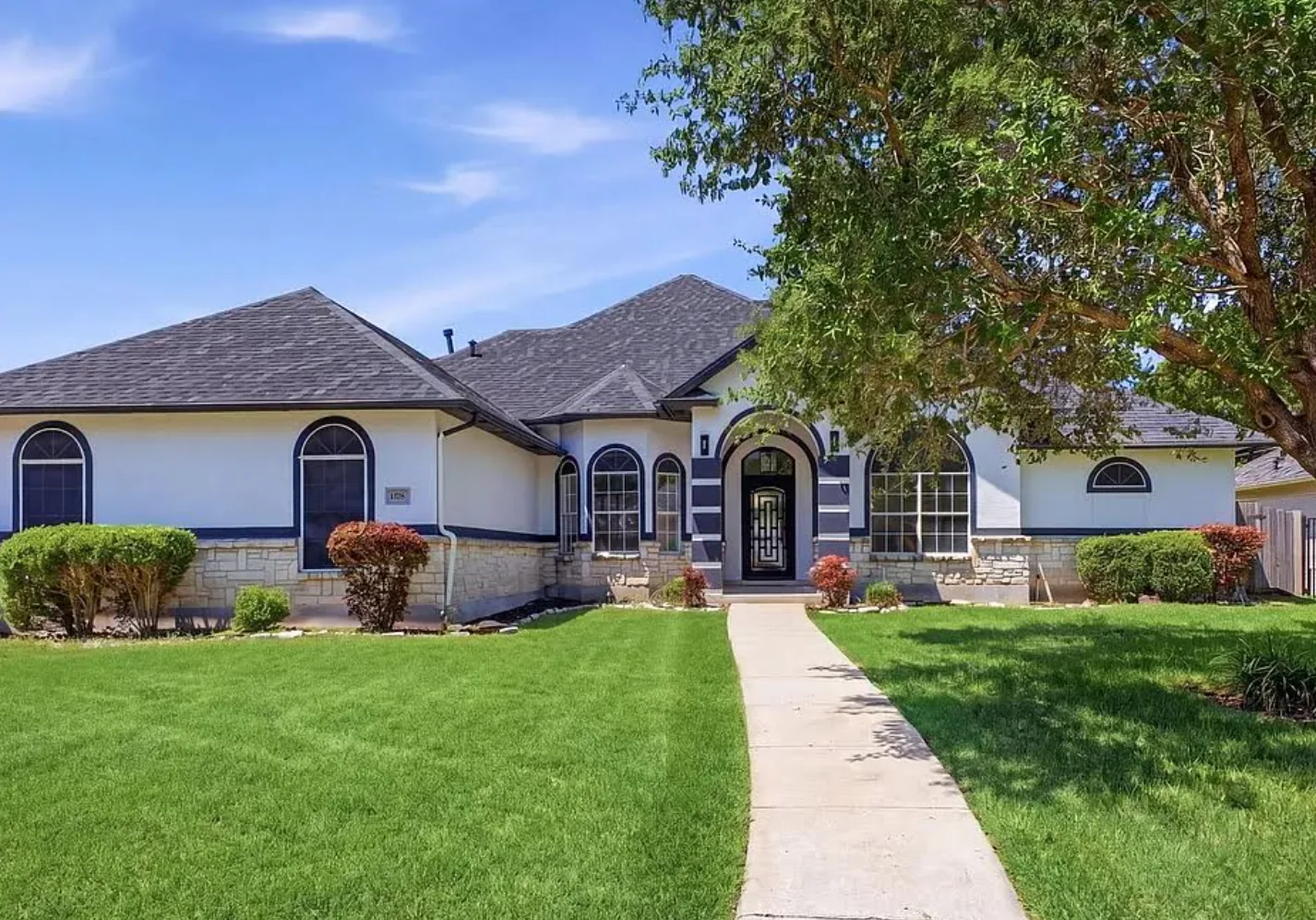 Finished single storey home in San Antonio with stone and stucco elevation, arched windows and an iron and glass front door