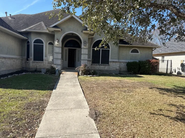 Front of the house before the remodel, faded green stucco, dark sun screens over the windows and a dry lawn