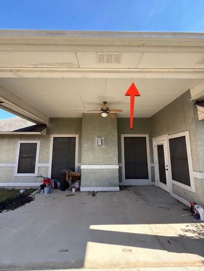 Covered patio before the remodel, weathered green stucco, a stained slab and building materials stacked against the wall