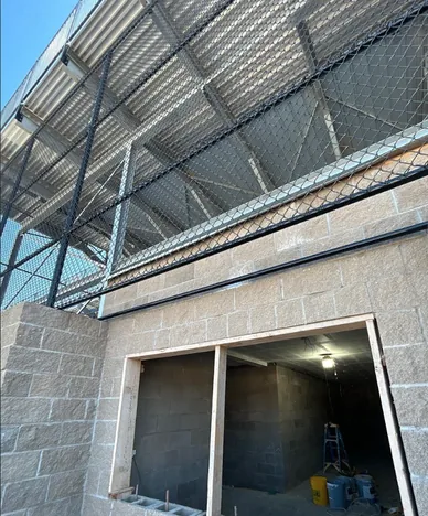 Chain link mesh panels fixed between steel posts along a block wall under a grandstand